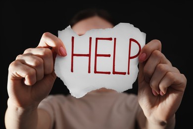 Photo of Woman holding piece of paper with word Help on black background, closeup. Domestic violence concept