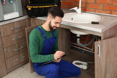 Male plumber with clipboard near kitchen sink. Repair service