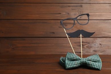 Paper moustache, glasses and bow tie on wooden background with space for text. Father's day celebration