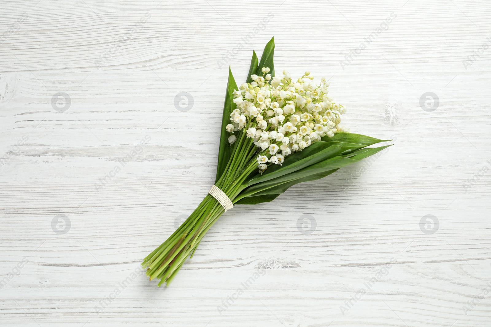 Photo of Beautiful lily of the valley bouquet on white wooden table, top view