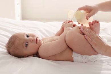 Photo of Woman applying massage oil onto skin of her baby on bed, closeup