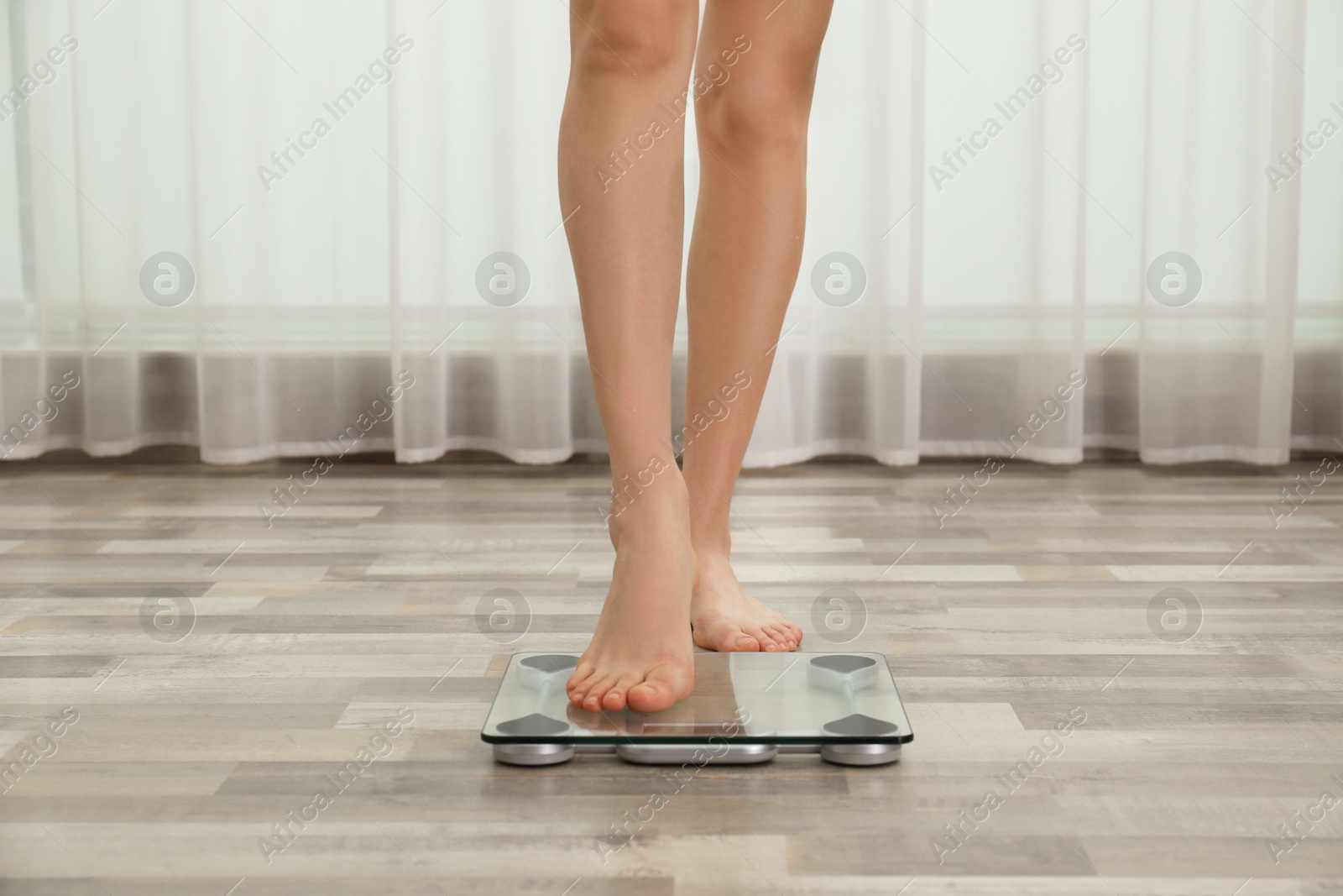 Photo of Woman stepping on floor scales indoors, closeup. Weight control