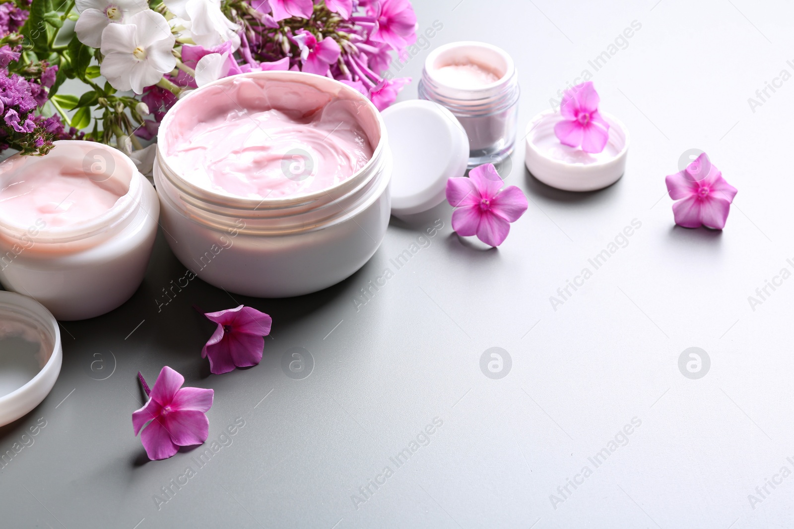 Photo of Jars of body cream and flowers on grey background. Space for text