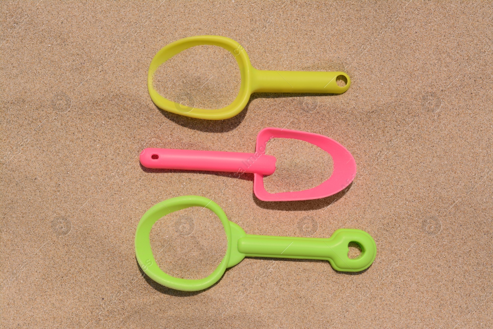 Photo of Colorful plastic shovels on sand, flat lay. Beach toys