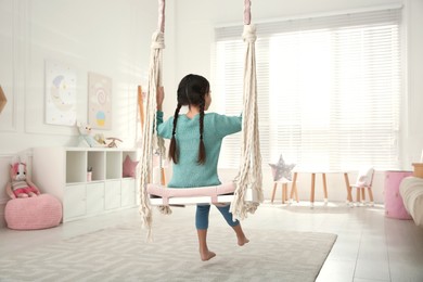 Photo of Cute little girl playing on swing at home, back view