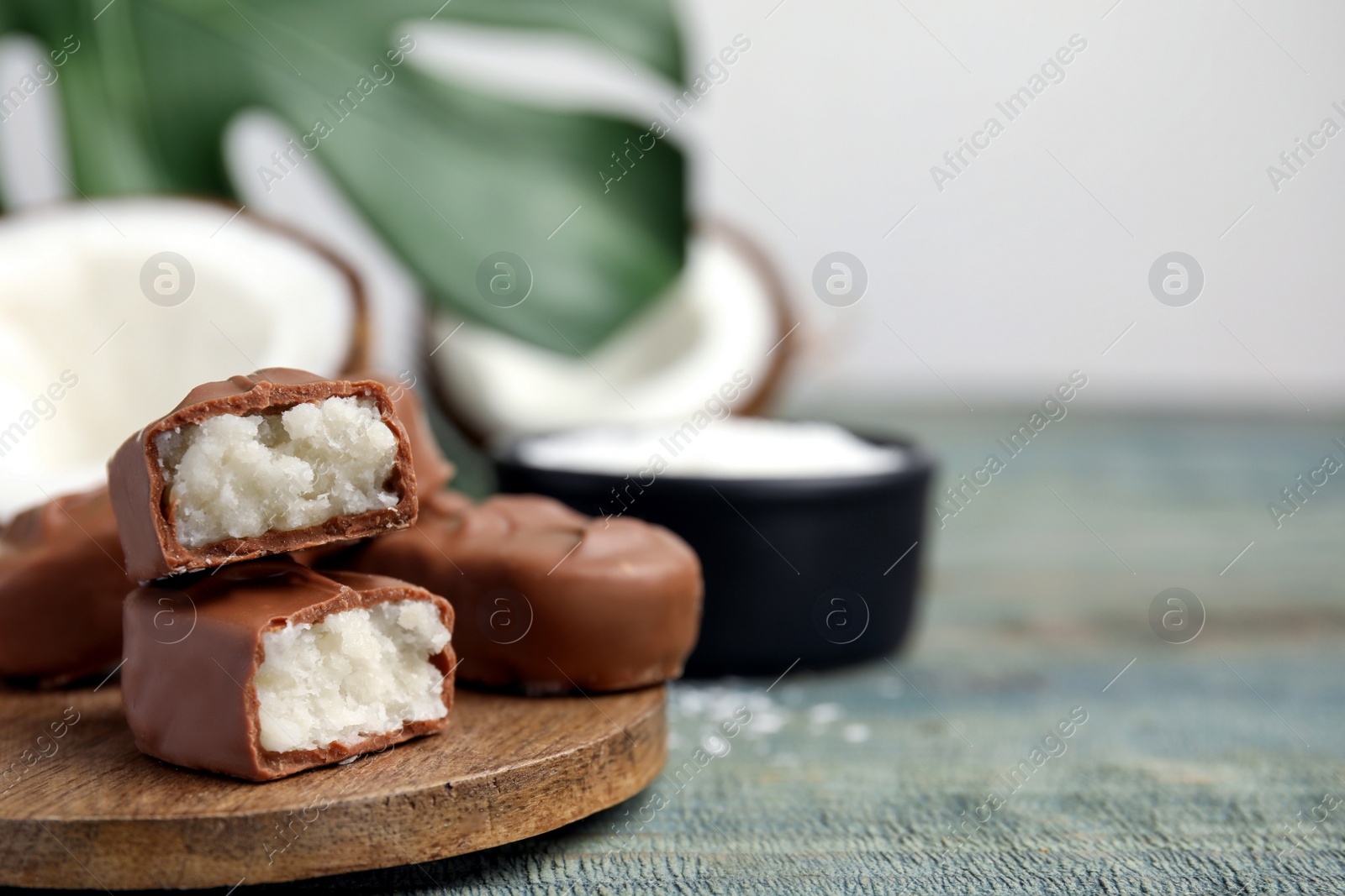 Photo of Delicious milk chocolate candy bars with coconut filling on blue wooden table, closeup. Space for text