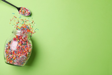 Photo of Colorful sprinkles, jar and spoon on green background, flat lay with space for text. Confectionery decor