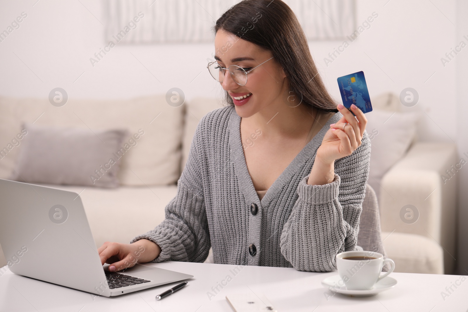 Photo of Woman with credit card using laptop for online shopping at white table indoors