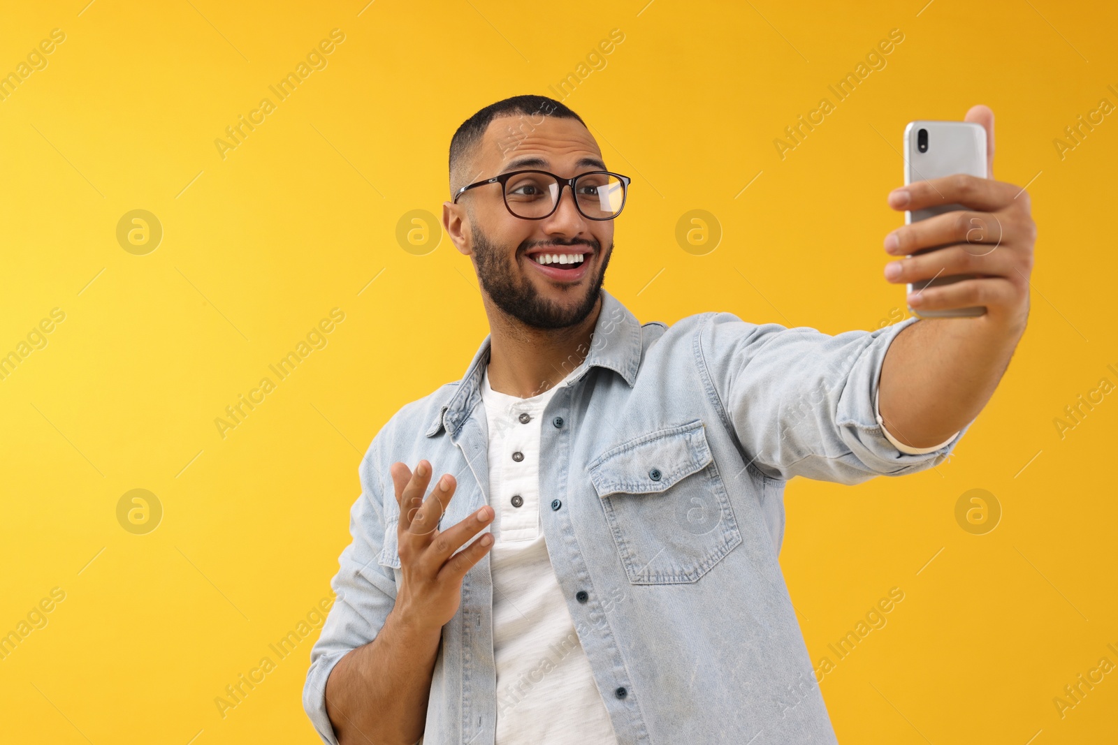 Photo of Smiling young man taking selfie with smartphone on yellow background