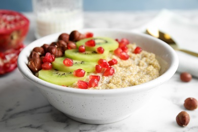 Photo of Bowl of quinoa porridge with hazelnuts, kiwi and pomegranate seeds on marble table