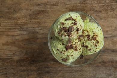 Photo of Delicious green ice cream served in dessert bowl on wooden table, top view. Space for text