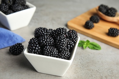 Bowl of tasty blackberries on grey table