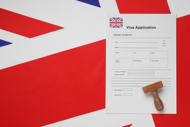 Immigration to United Kingdom. Visa application form and wooden stamp on flag, top view. Space for text
