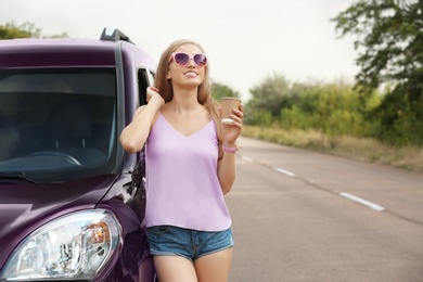 Photo of Young woman with cup of coffee near car on road. Joy in moment