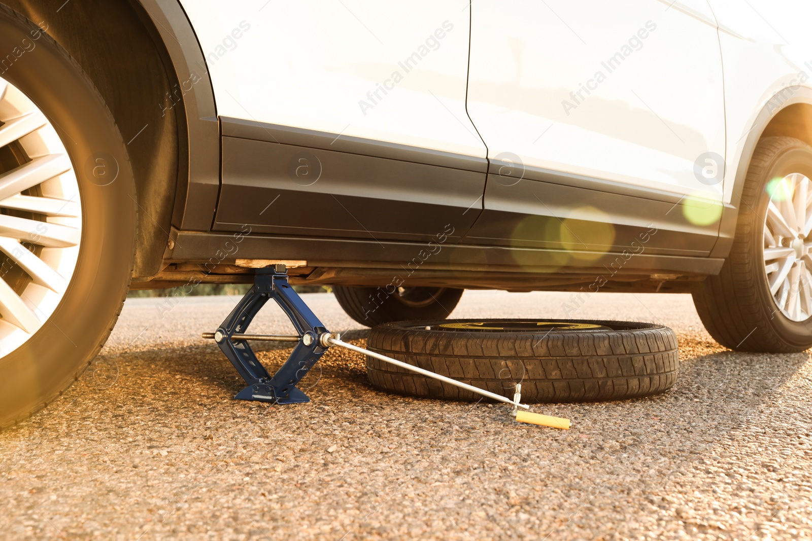 Photo of Car lifted by scissor jack and spare wheel on roadside