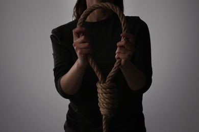 Photo of Woman holding rope noose on light background, closeup