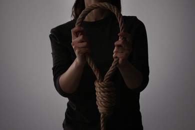 Woman holding rope noose on light background, closeup