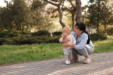 Mother teaching her baby how to walk outdoors. Space for text