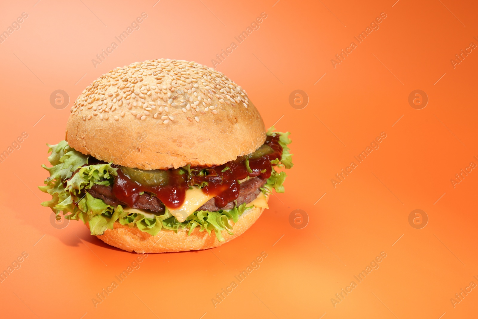 Photo of Delicious cheeseburger with lettuce, pickle, ketchup and patty on coral background. Space for text