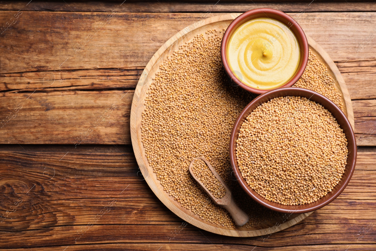 Photo of Mustard seeds and sauce on wooden table, top view. Space for text