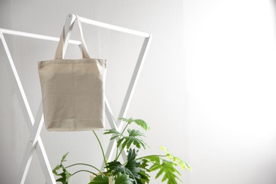 Photo of Houseplant and eco bag on rack near white wall. Space for design