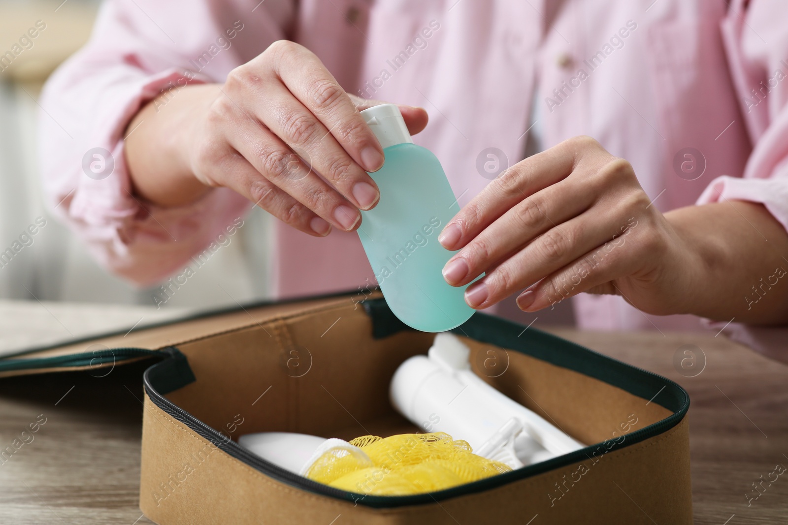 Photo of Woman packing cosmetic travel kit into compact toiletry bag at wooden table indoors, closeup. Bath accessories