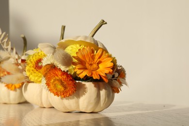 Small pumpkins with beautiful flowers and spikelets on white wooden table, closeup. Space for text