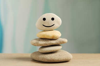Photo of Stack of stones with drawn happy face on table against light turquoise background, closeup. Zen concept
