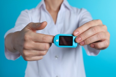Photo of Female doctor holding pulsimeter on color background, closeup. Medical object