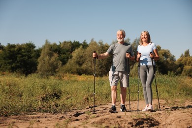 Photo of Senior couple with poles for Nordic walking outdoors on sunny day