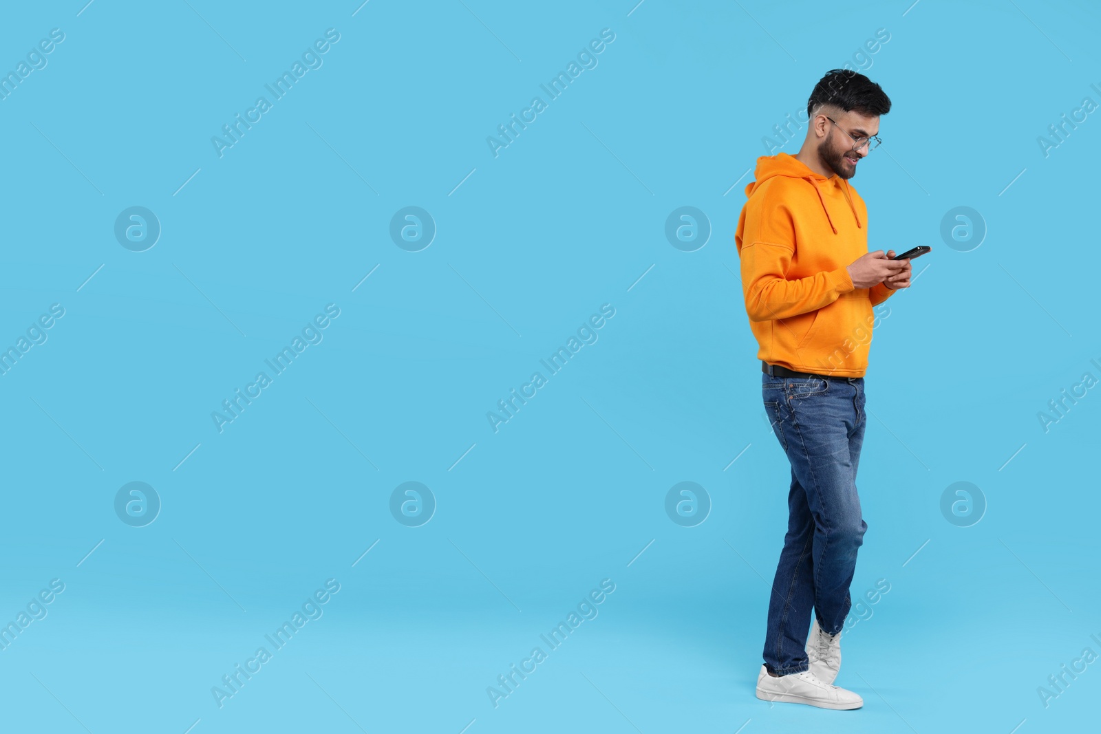 Photo of Happy young man using smartphone on light blue background, space for text