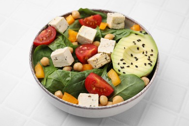 Bowl of tasty salad with tofu and vegetables on white tiled table, closeup