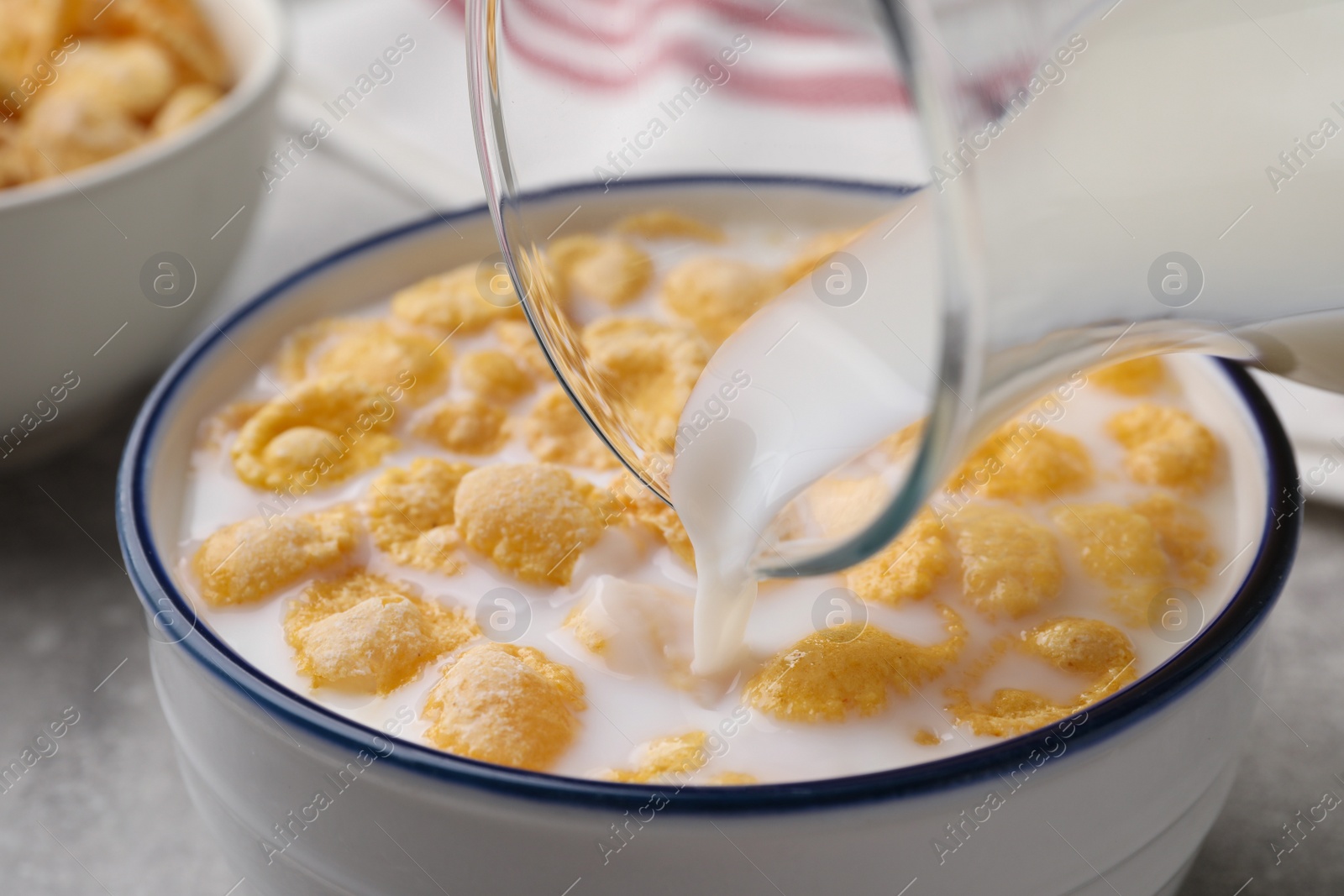 Photo of Pouring milk into bowl with cornflakes on table, closeup