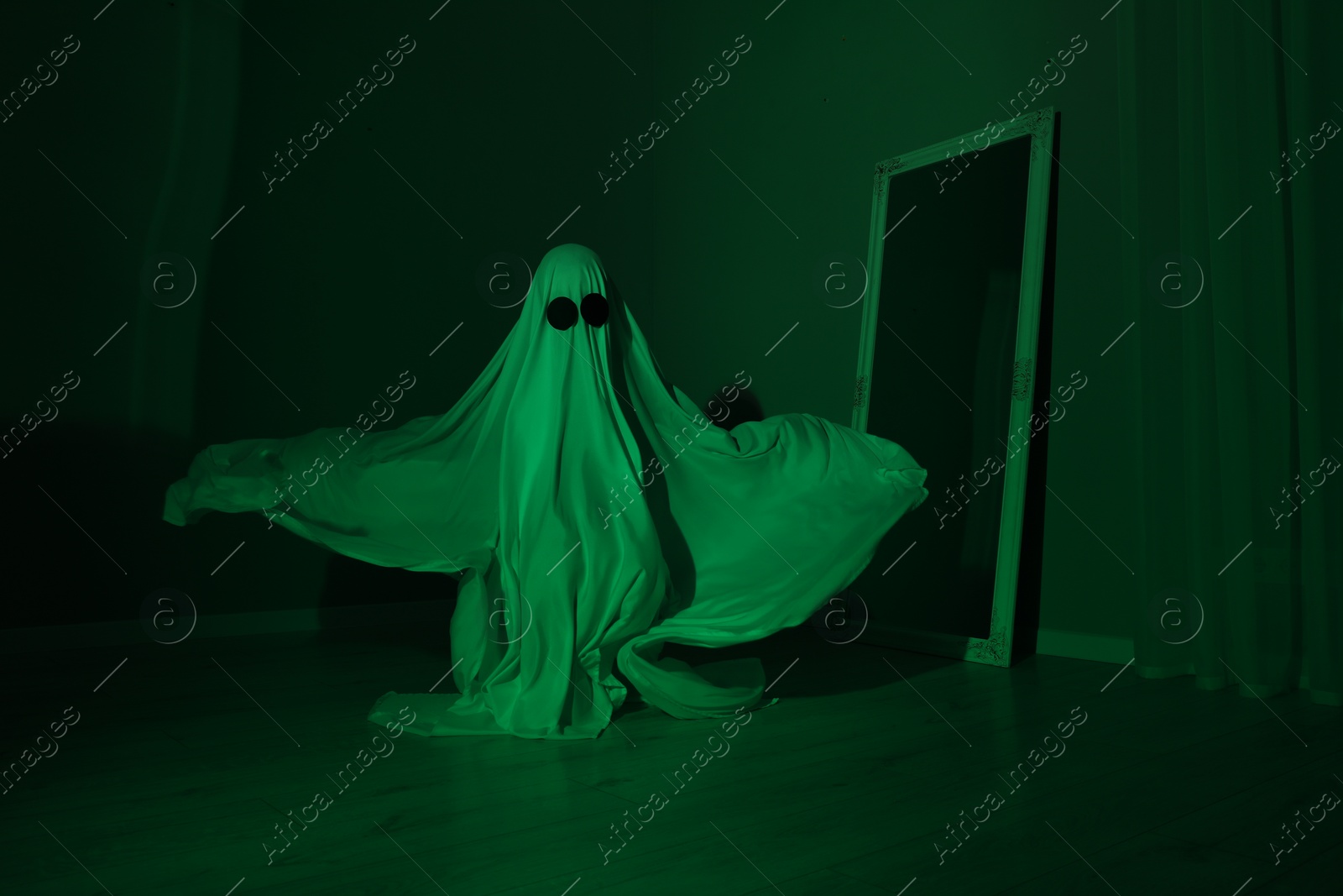 Photo of Creepy ghost. Woman covered with sheet in green light