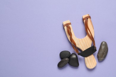 Wooden slingshot with stones on violet background, flat lay. Space for text