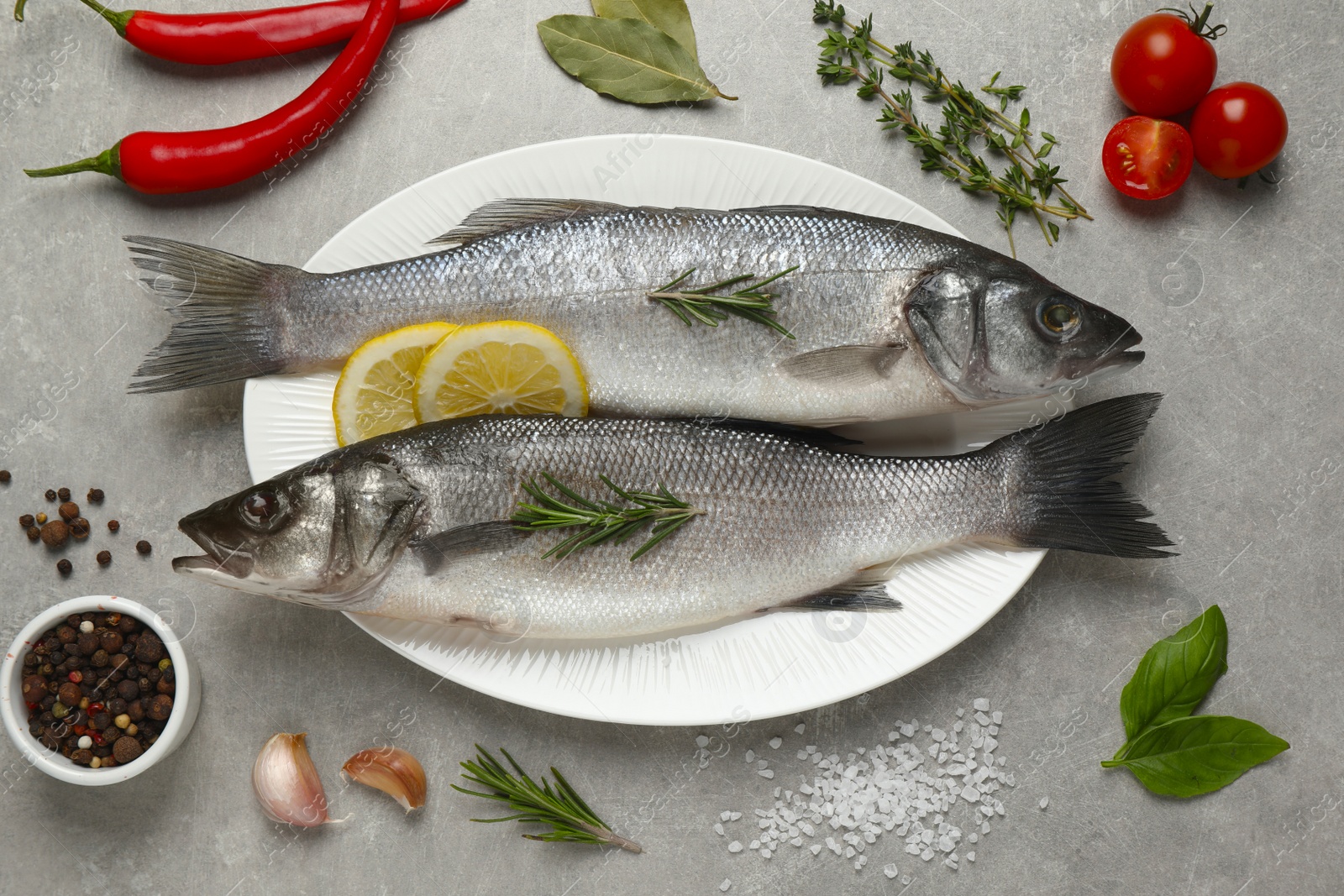 Photo of Sea bass fish and ingredients on grey table, flat lay