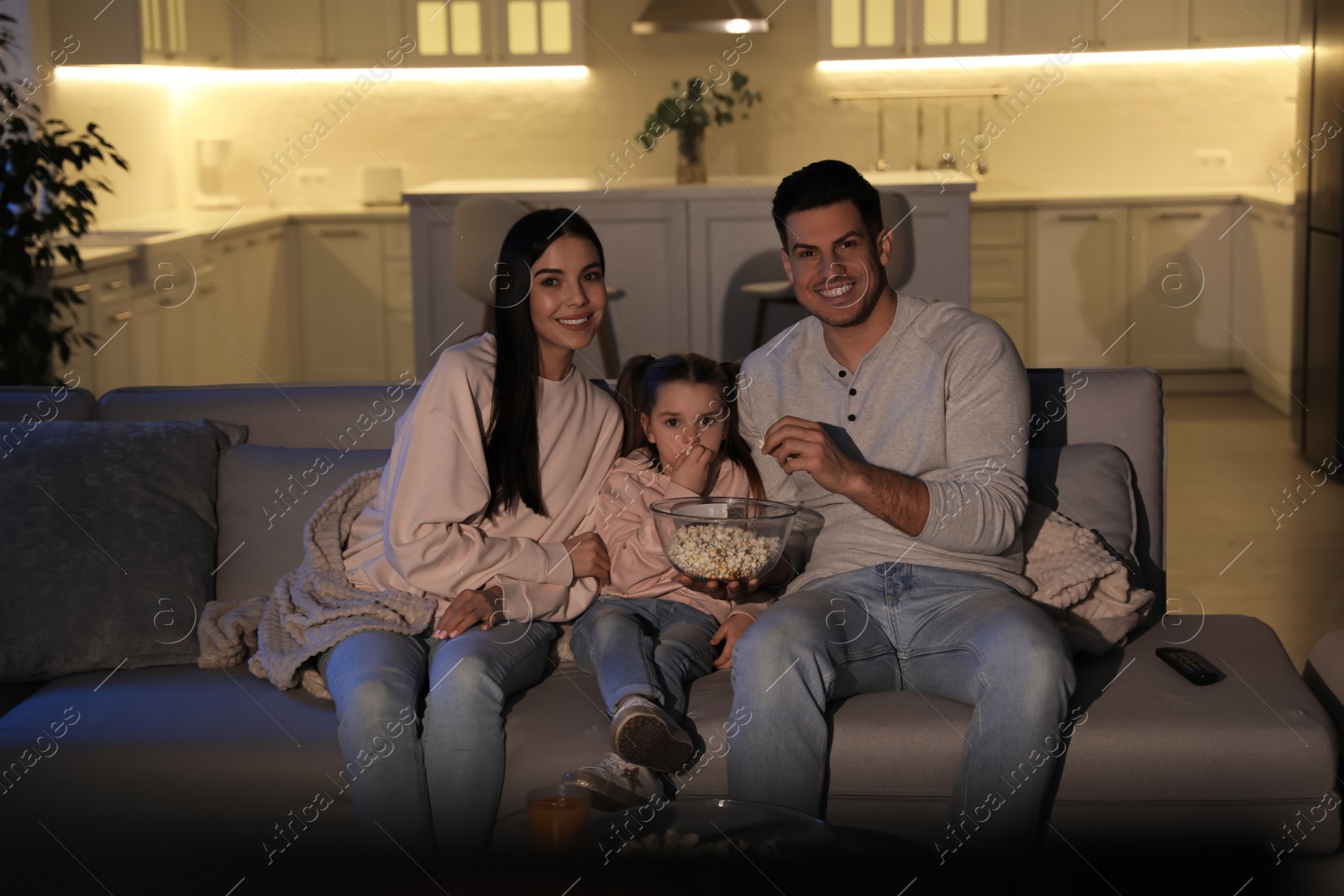 Photo of Family watching movie with popcorn on sofa at night