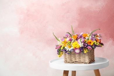 Photo of Wicker basket with beautiful wild flowers on table against color background