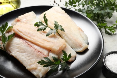 Photo of Plate with raw cod fish and parsley on table, closeup