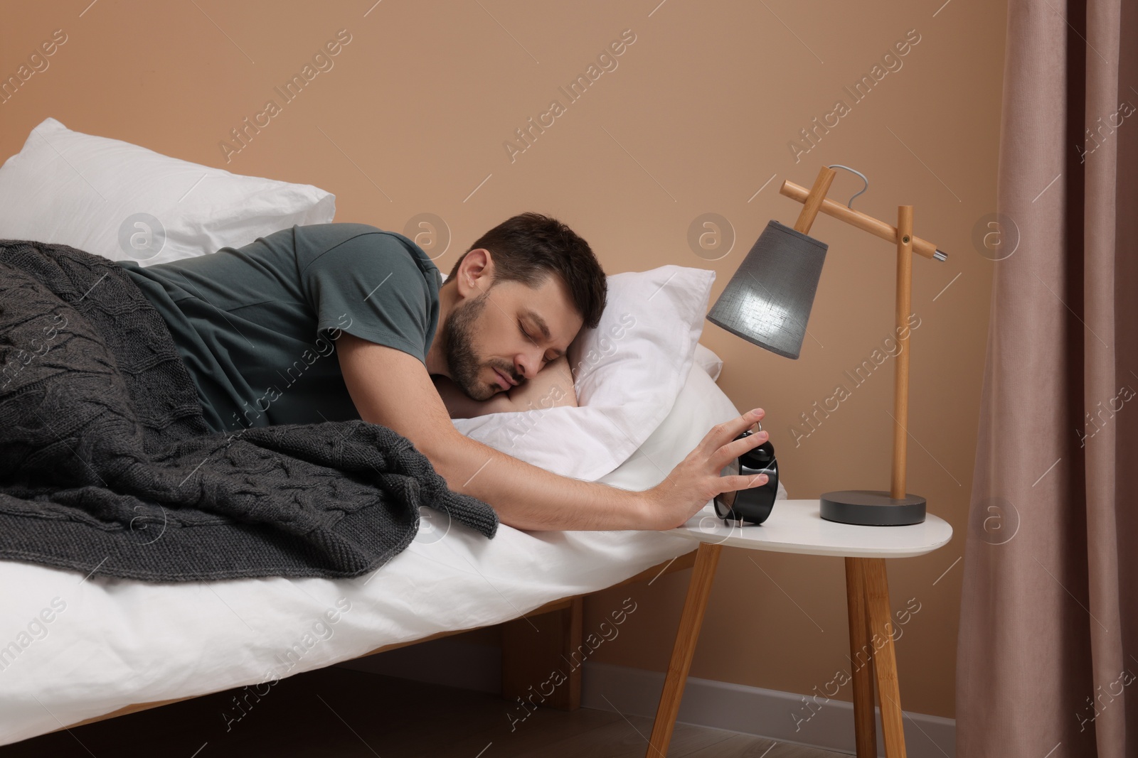 Photo of Sleepy man turning off alarm clock on nightstand in morning