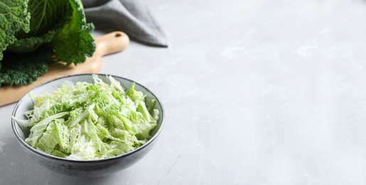Photo of Cut fresh savoy cabbage in bowl on light table, closeup. Space for text