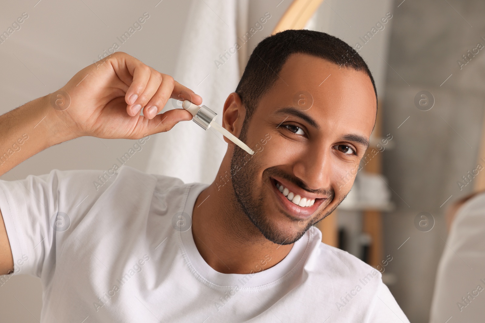 Photo of Handsome man applying cosmetic serum onto face in bathroom