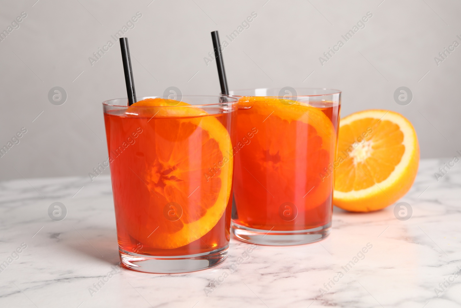 Photo of Aperol spritz cocktail, orange slices and straws in glasses on white marble table