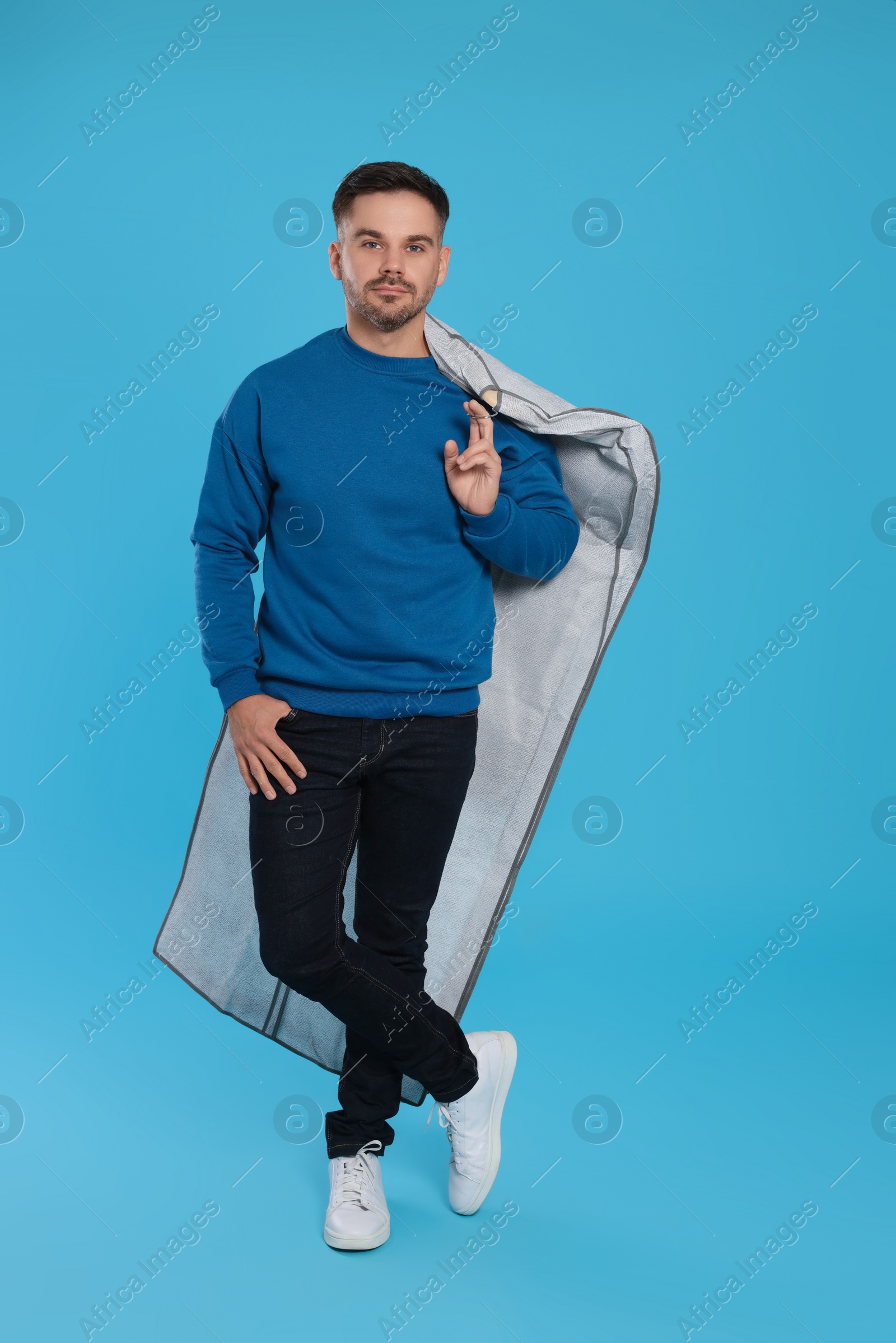 Photo of Man holding garment cover with clothes on light blue background. Dry-cleaning service