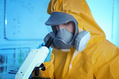 Photo of Scientist in chemical protective suit using microscope at laboratory. Virus research