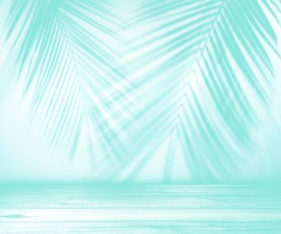 Image of Turquoise wooden table against light background with shadows of palm branches. Summer party