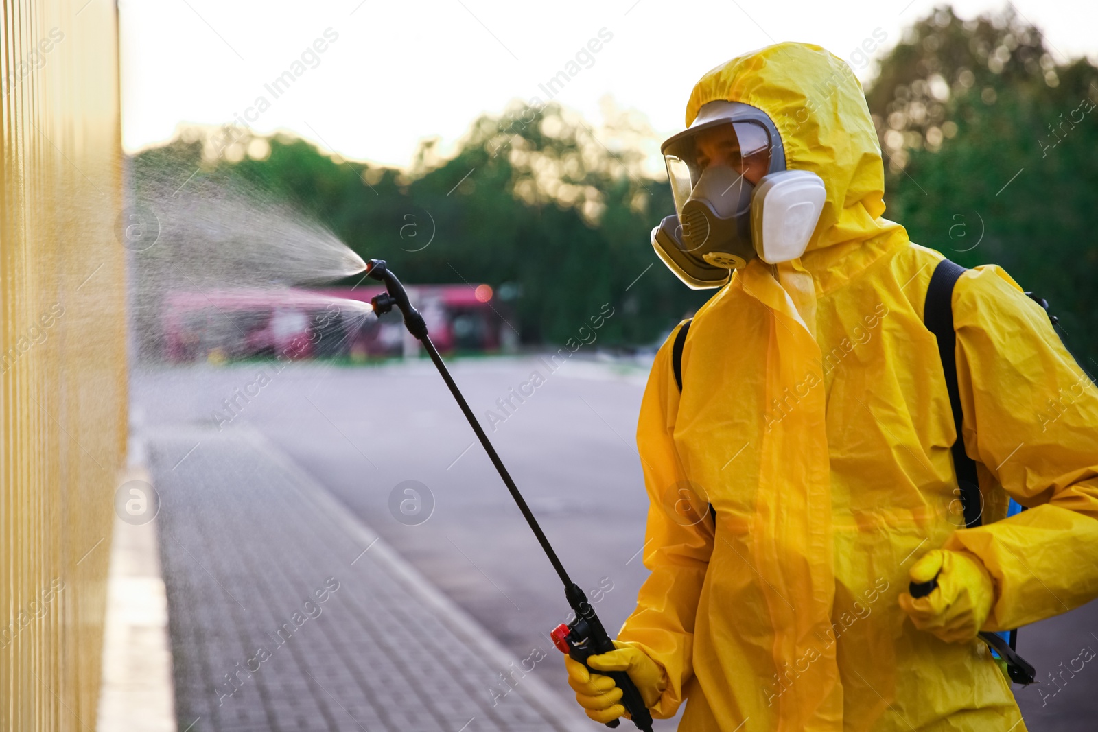 Photo of Person in hazmat suit disinfecting street with sprayer. Surface treatment during coronavirus pandemic