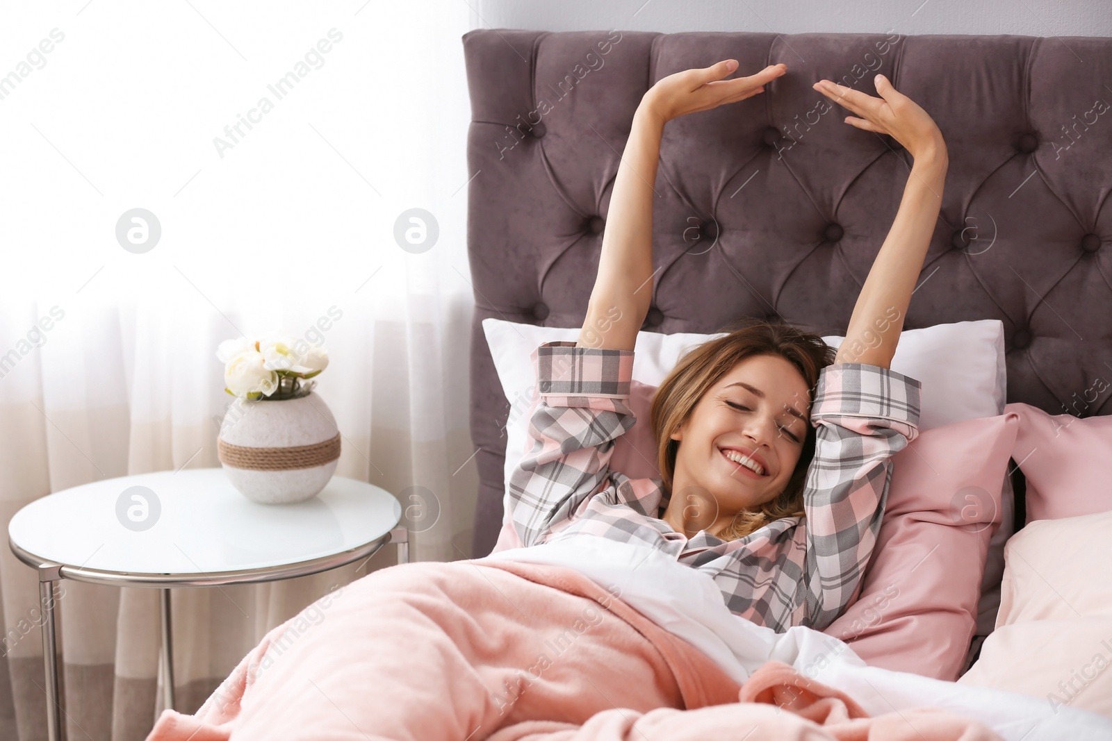 Photo of Young beautiful woman stretching after sleeping in bed at home