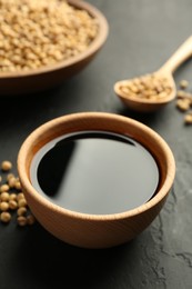 Tasty soy sauce in bowl and soybeans on black table, closeup