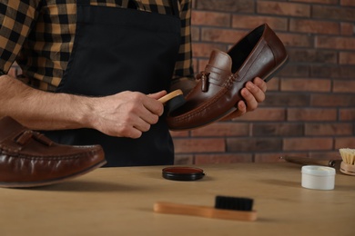 Photo of Craftsman taking professional care of brown leather shoes in workshop, closeup